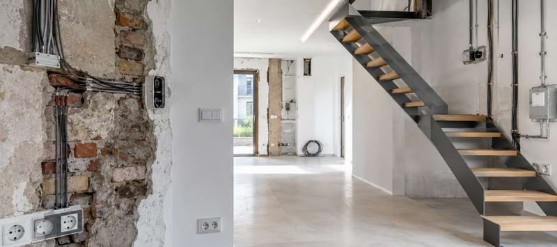 Offener Raum mit Sicht auf eine moderne Treppe, unvollendeten Wänden und Elektroinstallationen. Minimalistische Gestaltung.